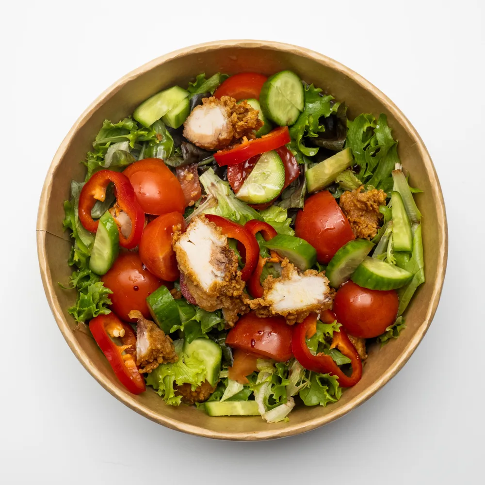 A colorful bowl of chicken salad with lettuce, cucumber, peppers, and tomatoes