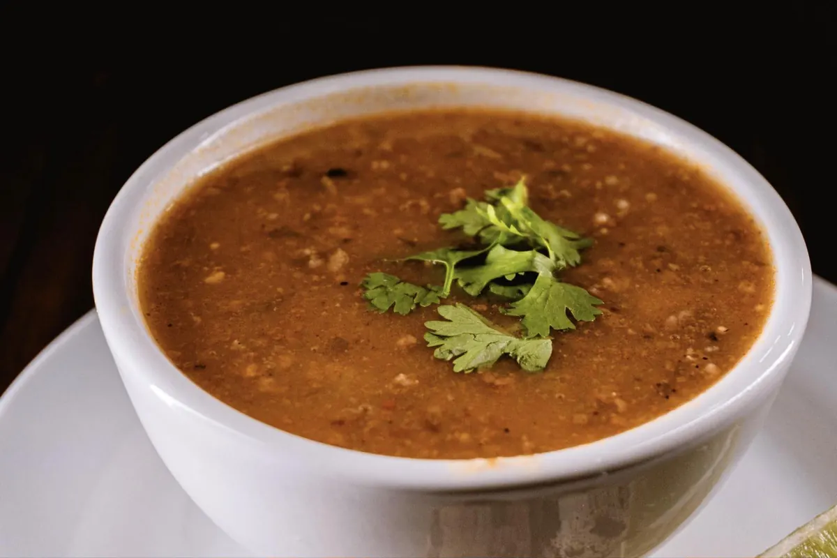 A white bowl of lentil soup garnished with cilantro leaves