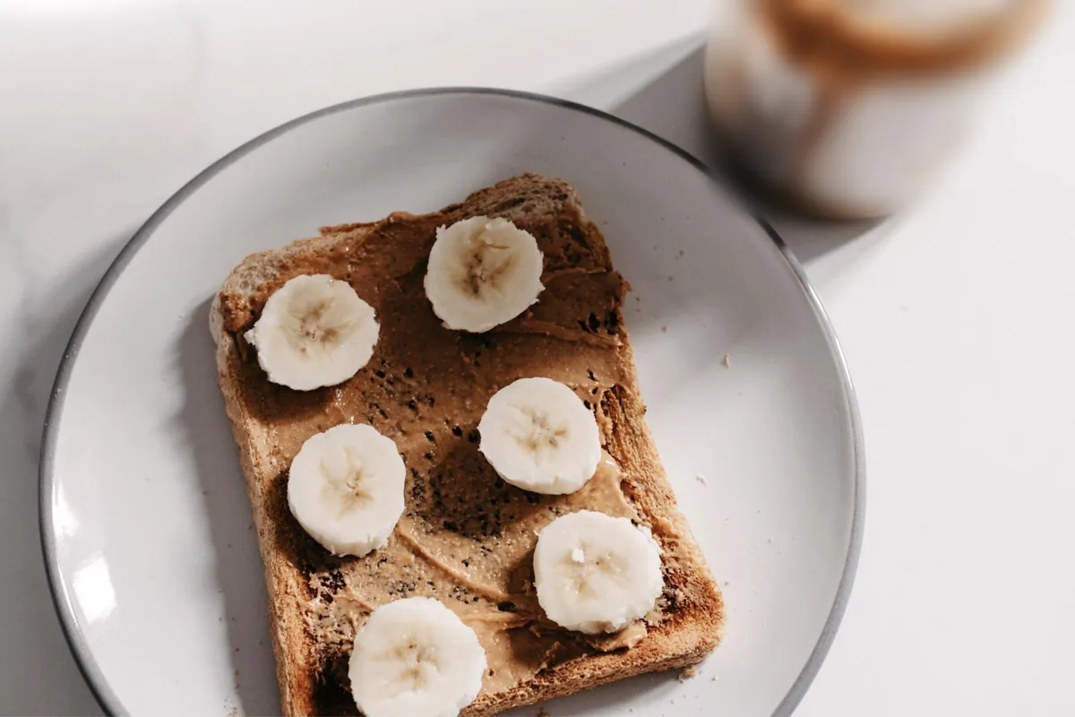 A slice of toast spread with peanut butter and topped with banana slices on a white plate