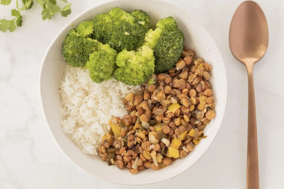 A white bowl of spiced lentils, white rice, and steamed broccoli beside a copper spoon