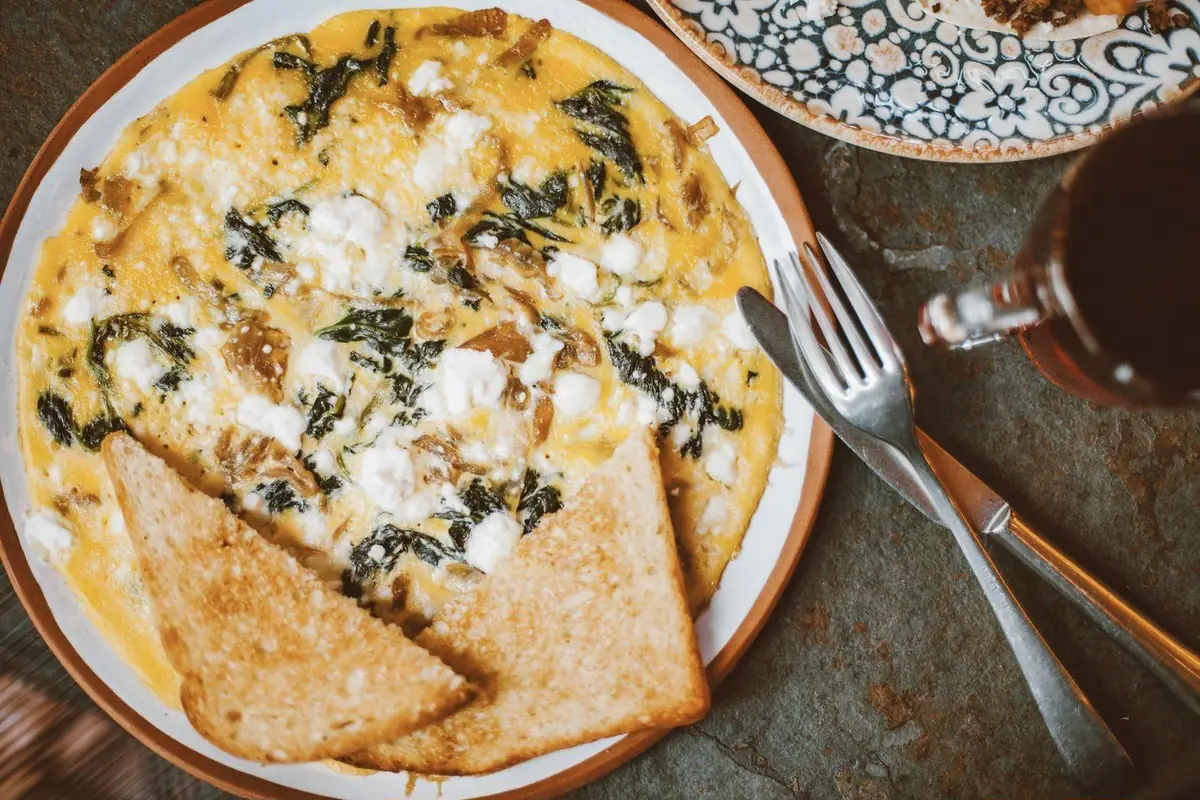 An omelette with spinach, onion, and crumbled white cheese on a plate with two triangles of toast