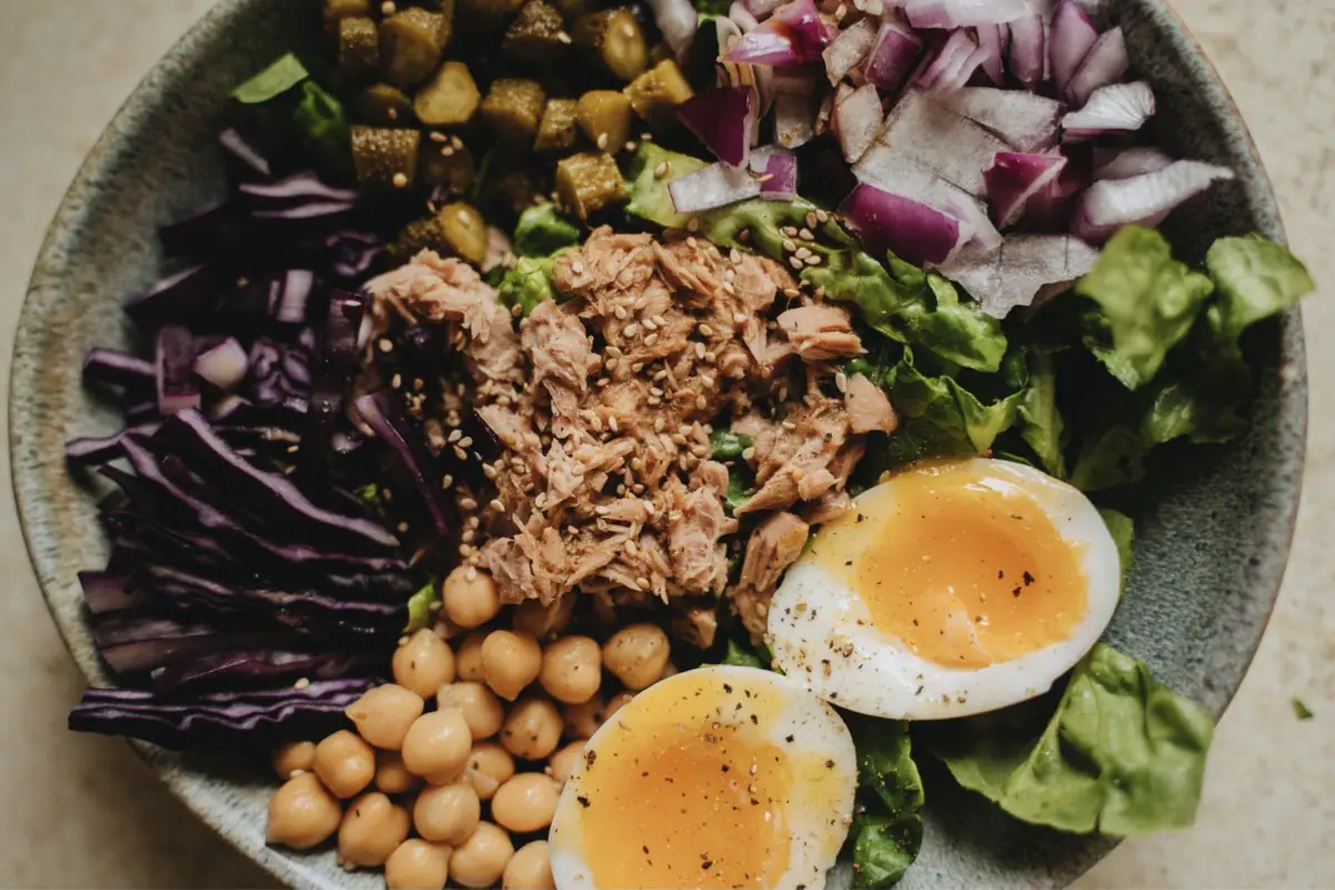 A salad bowl with tuna, chickpeas, soft-boiled eggs, lettuce, red cabbage, and onion